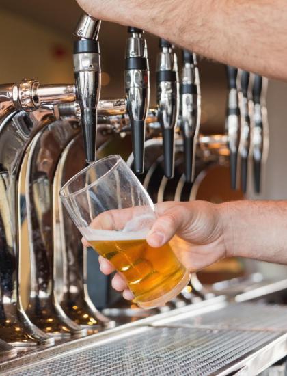 Mano che versa birra da un rubinetto in un bicchiere.