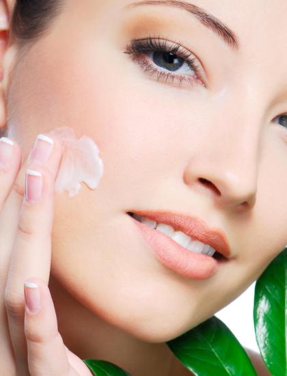 Woman applying cream on face with green leaves.