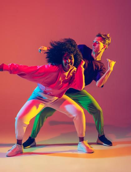 Two people dance energetically against a colorful background.