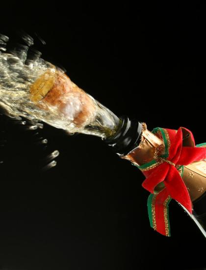 Champagne cork flying, bottle decorated with red bow.