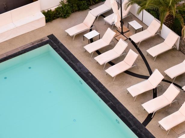 Pool with white loungers and closed umbrellas, aerial view.